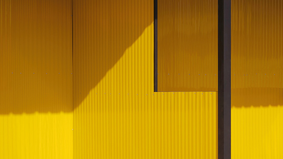 Yellow aluminium steel wall with black metal column of two street kiosks structure in under construction with sunlight and shadow on surface, perspective side view