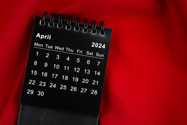 istock April 2024 Black spiral desktop calendar on red textile. 1961430933