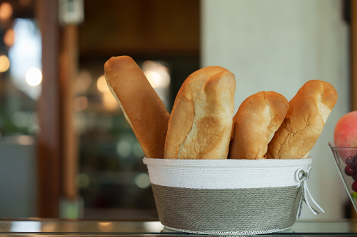 There is a yellow-brown bakery bakery baguette in a gray-white cloth basket. Appetizing bread is placed on the counter inside a minimalist coffee shop and small business.