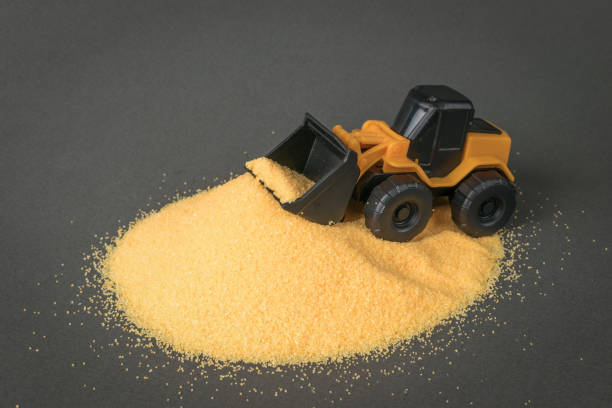 A big yellow bulldozer shoveling sand into a big pile. A car for a construction company.