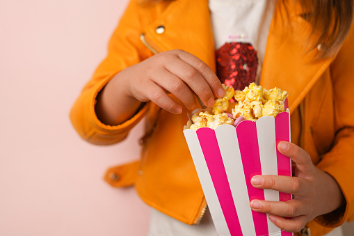 The girl is eating caramel popcorn from Striped carton bucket, close-up