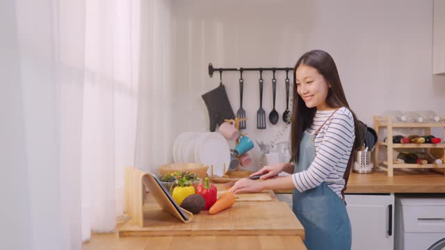 Asian young attractive woman making green salad for breakfast in morning. Beautiful girl wear apron enjoy eat clean vegetables healthy food for health care in house. Diet lose weight and foods concept