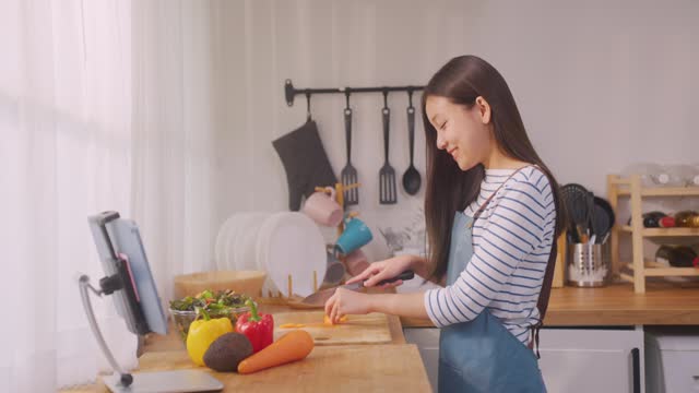 Asian young attractive woman making green salad for breakfast in morning. Beautiful girl wear apron enjoy eat clean vegetables healthy food for health care in house. Diet lose weight and foods concept