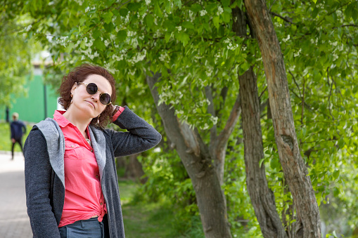 Portrait of a mature woman in sunglasses against the background of green trees in the park.