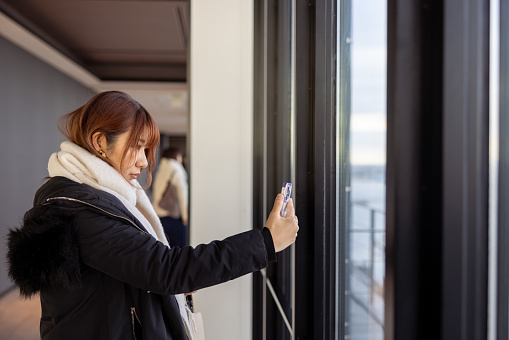 Female tourist taking photos of cityscape from observatory floor in high raised building