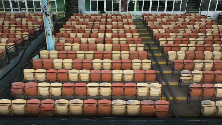 Drone, aerial, video of old faded orange and yellow painted wooden seats at a abandoned a stadium grandstand.