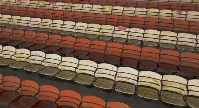 Drone, aerial, video of old faded orange and yellow painted wooden seats at a abandoned a stadium grandstand.