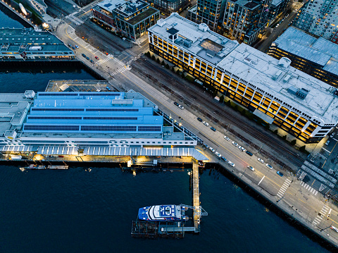 The Seattle Port Building has solar panels on its roof.  The FRS Clipper is moored which takes tourists in the Salish Sea.  A parking garage is across the street from the Port building.  The aerial view is along the waterfront in Seattle Washington Pier 70.