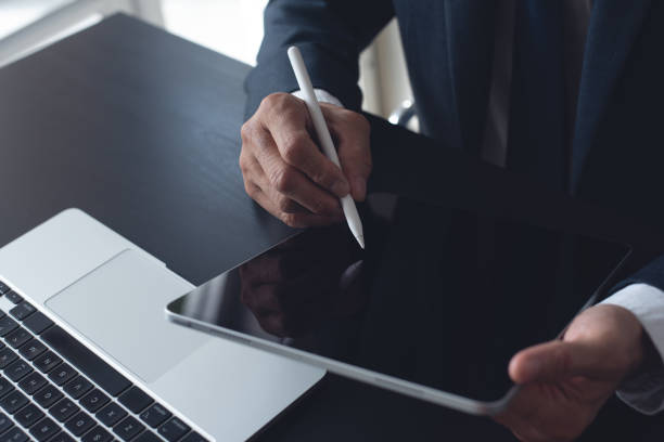 istock Close up, businessman using stylus pen signing e-document on digital tablet at office, E-signing, electronic signature concept. Business man online working on computer devices on office desk 1961732591