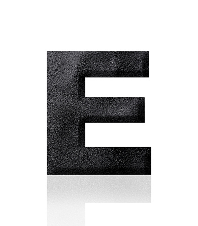 Close-up of three-dimensional black sand alphabet letter E on white background.