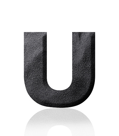 Close-up of three-dimensional black sand alphabet letter U on white background.
