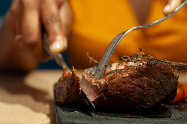 person carving succulent grilled steak on a sizzling hot plate at dinner - steak plate gourmet beef imagens e fotografias de stock