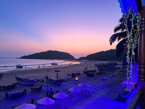 Palolem Beach, Goa, India - January, 11 2024: Stock photo showing view from beach restaurant of Goa coastline in silhouette against the tropical orange, pink and purple sunset sky at Palolem Beach, Goa, India.
