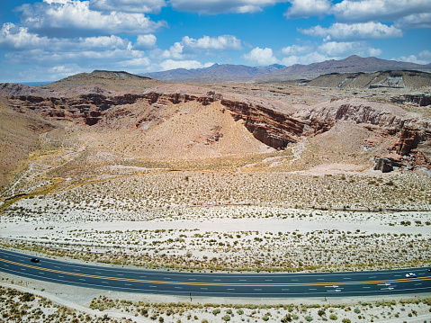 Empty road through desert surrounded by mountains, under a sky adorned with clouds