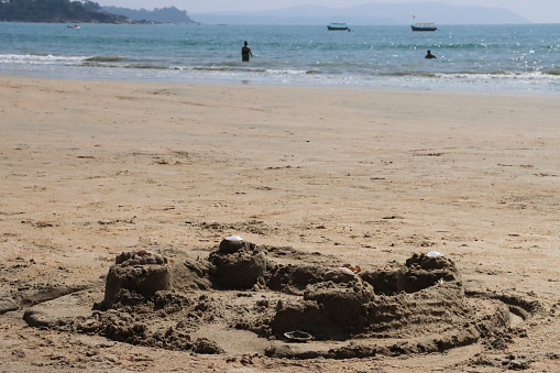 Stock photo showing close-up view of a complex sandcastle built on a sunny, golden sandy beach with sea at low tide in the background. Summer holiday, tourism and activities concept.