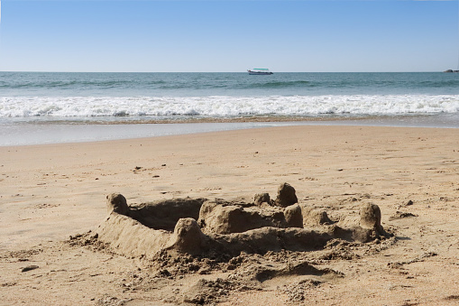 Stock photo showing close-up view of a complex sandcastle built on a sunny, golden sandy beach with sea at low tide in the background. Summer holiday, tourism and activities concept.