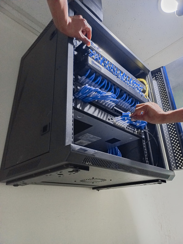 A network technician is setting up and configuring the patch panel and router switch in the wall-mounted cabinet.
