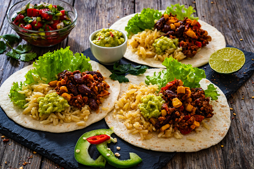 Chili con carne with rice on tortilla on wooden background