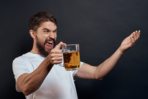 Man with a mug of beer in his hands emotions fun lifestyle white t-shirt dark isolated background. High quality photo