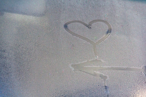Symbol heart sign and arrow of a raindrop on a foggy glass. Symbol concept path to love and happiness.