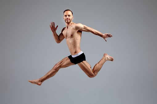 Full length portrait of a confident young sportsman shirtless jumping isolated over white background.