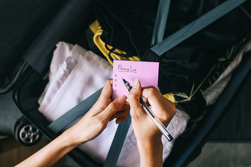 Hand Writing Packing List on Paper Notes Against Travel Baggage Background
