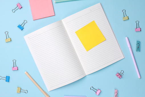 Yellow Color Paper Notes on Pages of  Book with Pastel Colored Clips on Blue Background