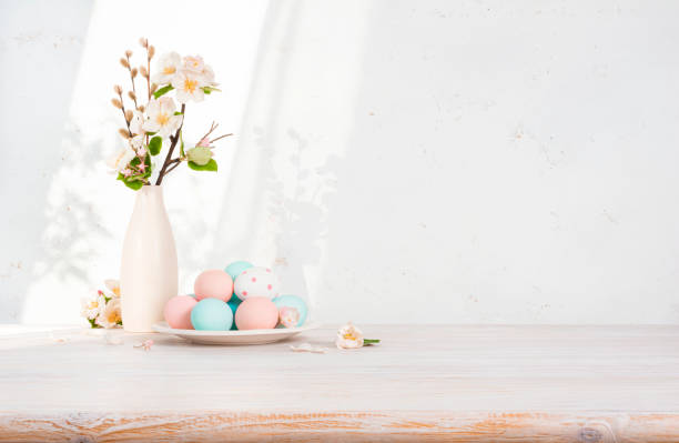 istock Wooden table top with easter eggs on plate, flowers and shadows on abstract kitchen wall background 1961880034