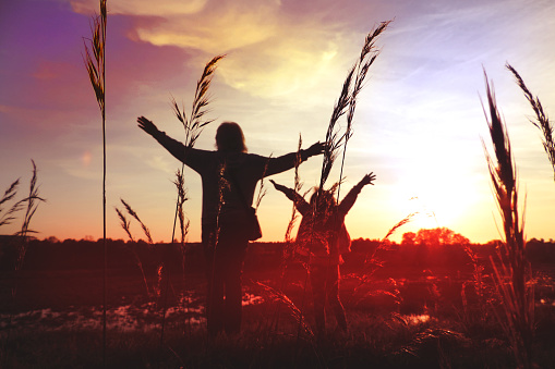 Child girl with mother in the meadow with raised hands, rear view. Relaxing. Summer sunset. Enjoying Life