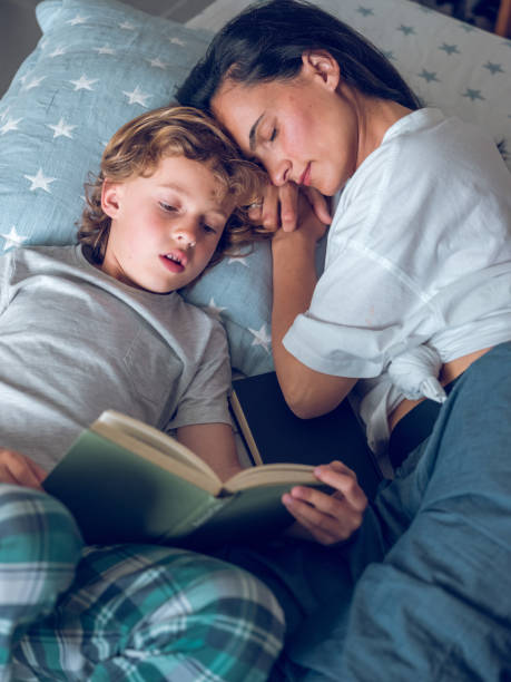 istock Little boy reading book near napping mom lying on bed 1961889901