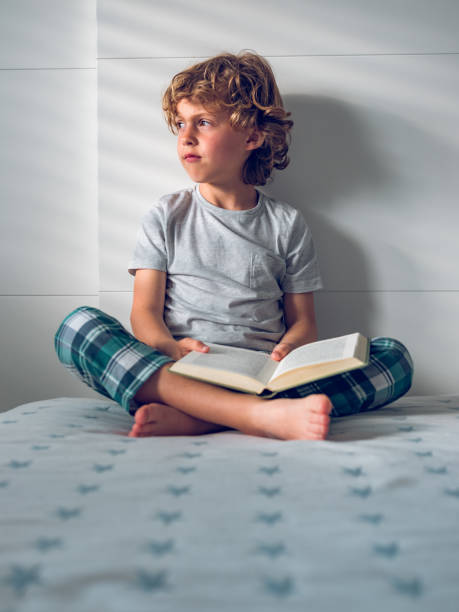 istock Pensive little boy sitting on bed with opened book 1961893037