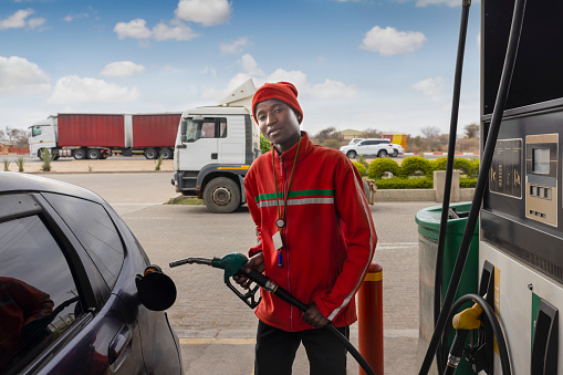 african american attendant at a petrol station holding the pump nozzle , filling a small car tank with gas