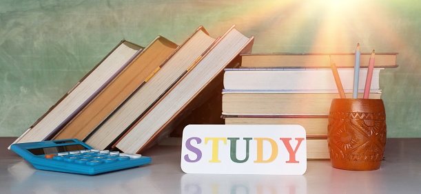 stack of textbooks and study card on desk over blurred blackboard in classroom