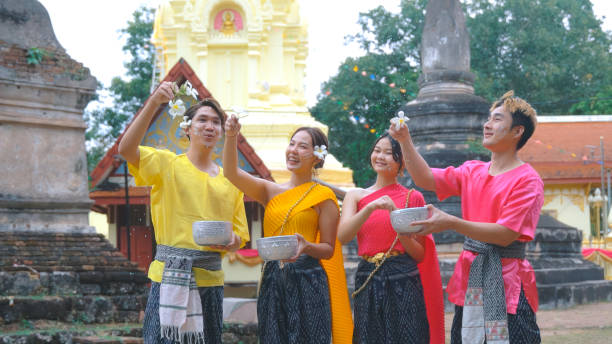 grupo feliz de jovens vestidos com roupas tradicionais tailandesas estão brincando na água durante o festival tailandês songkran. - buddhist new year songkran traditional festival dancing - fotografias e filmes do acervo