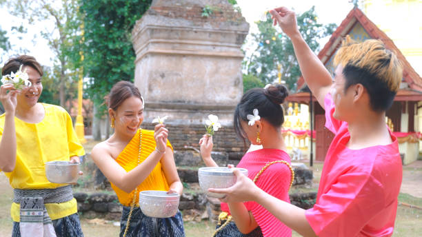 grupo feliz de jovens vestidos com roupas tradicionais tailandesas estão brincando na água durante o festival tailandês songkran. - buddhist new year songkran traditional festival dancing - fotografias e filmes do acervo