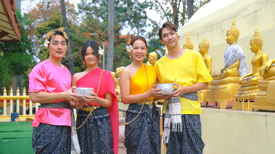 A group of young people and couples wearing traditional Thai water splash costumes during the Songkran Festival and a ceremony to bathe Buddha images in the Thai style Songkran Festival.