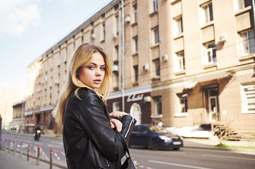 A woman in a black jacket walks down the street in the city cropped view. High quality photo