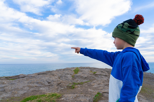 Boy on a cliff pointing to the sea