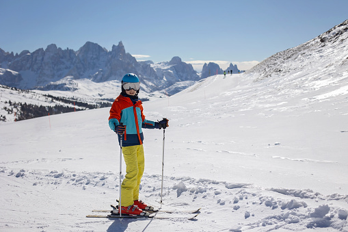 Cute 10 years old boy skier learning to ski down the slope in bright green outfit on sunny day