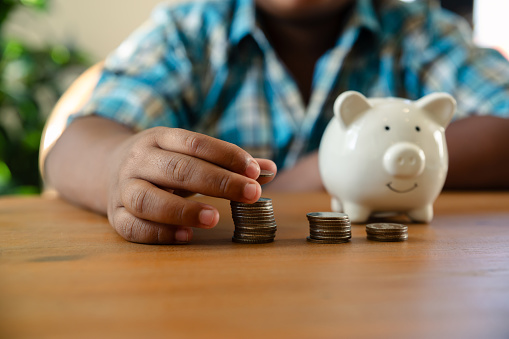 Little African boy counts money into piggy bank, Saving money concept.