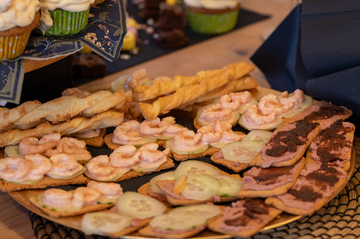 A gold plate of Hors d'oeuvres, appetisers at a part of Melba toast with prawns, pate and cucumber and pate and chutney with puff pastry cheese twists in the background