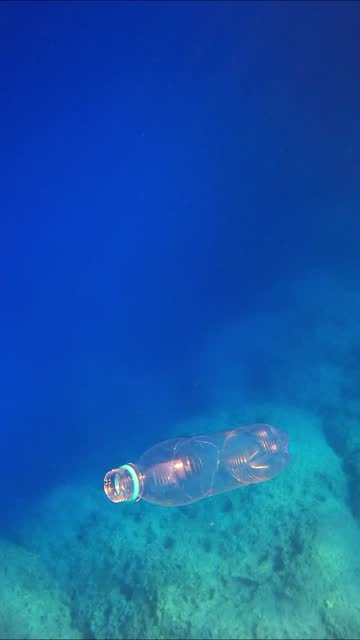 Transparent disposable plastic bottle sinks in blue water sinking to rocky seabed