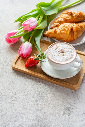 Happy mother's day, beautiful breakfast, lunch with cup of coffee (cappuccino) fresh croissants, strawberries on tray, bouquet of tulips as gift.