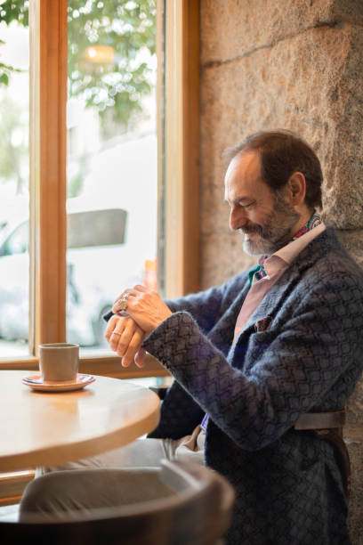 istock Senior man looking at the time on his watch while drinking coffee sitting in a cafe 1962030180