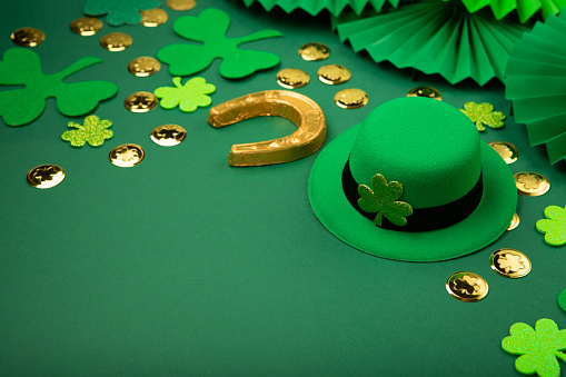 St. Patrick's Day leprechaun hat, gold coins and shamrocks on green background. Irish traditional holiday concept, copy space.