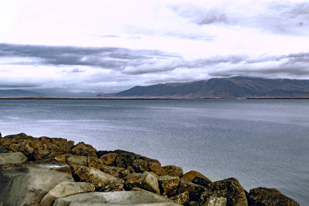 Scenic view of stone fence on highland overlooking calm rippling seawater and with rocky mountain range under cloudy blue sky in evening daylight