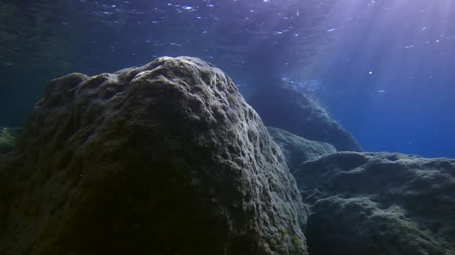 Large boulders in shallow water under bright rays of sun, Slow motion