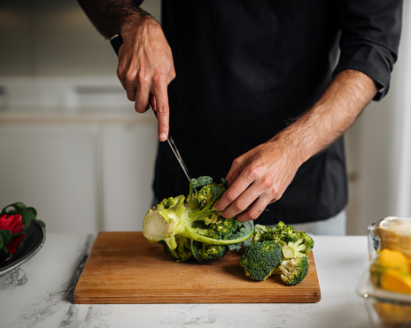 Chef cutting broccoli on a wooden board preparing healthy meal