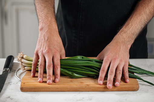 Chef preparing food with spring onion on wooden cutting board