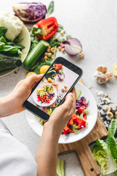istock A woman photographs a fresh vegetable salad on the kitchen table. 1962068344